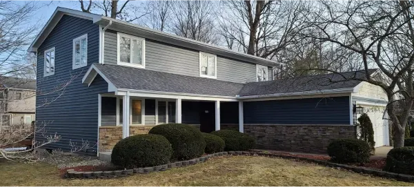 A blue and gray house with a porch and bushes in front of it.