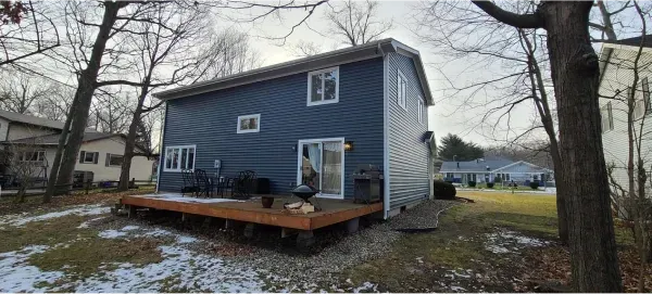 A small blue house with a deck in the backyard surrounded by trees.