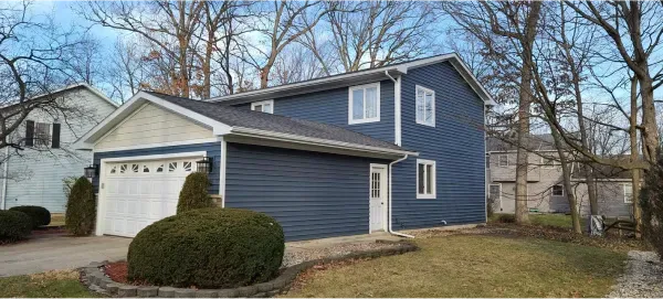 A blue and white house with a garage and trees in the background.