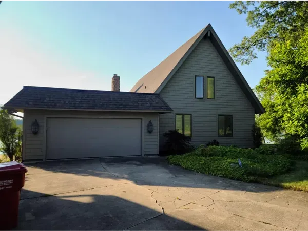 A house with a garage and a red trash can in front of it