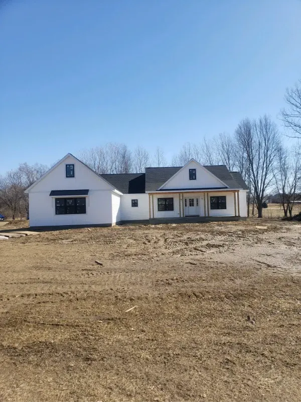 A white house is sitting in the middle of a dirt field.