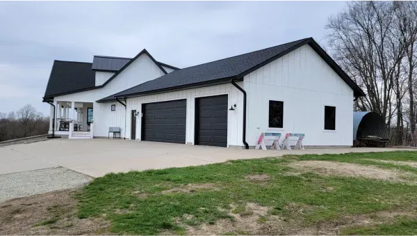 A white house with a black roof is sitting on top of a lush green field.