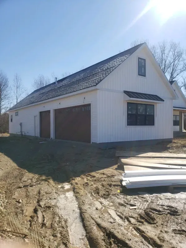 A white house with two garage doors is being built in the dirt.