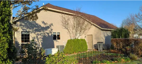 A brick house with a brown roof is surrounded by trees and bushes.