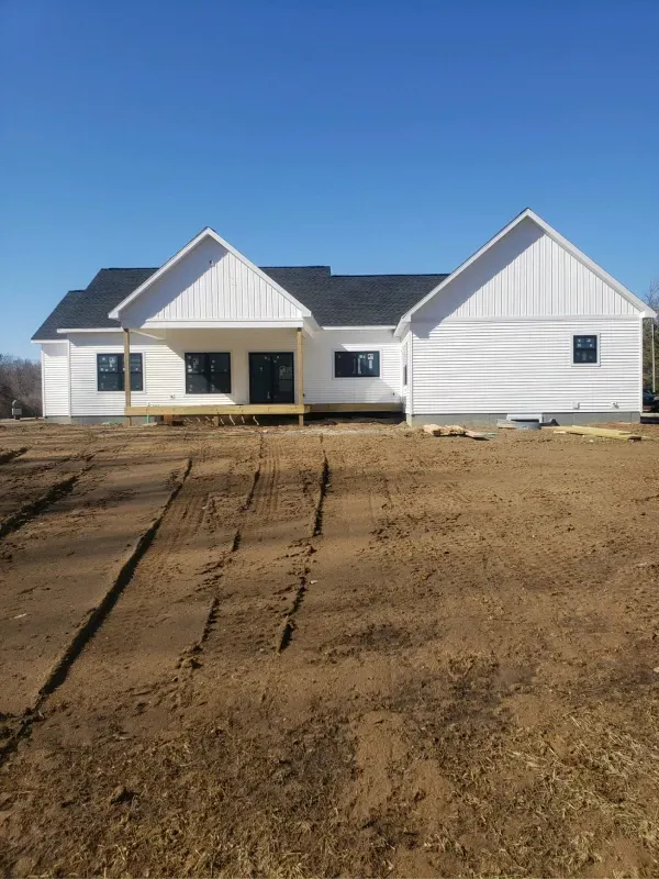 A white house is sitting in the middle of a dirt field.
