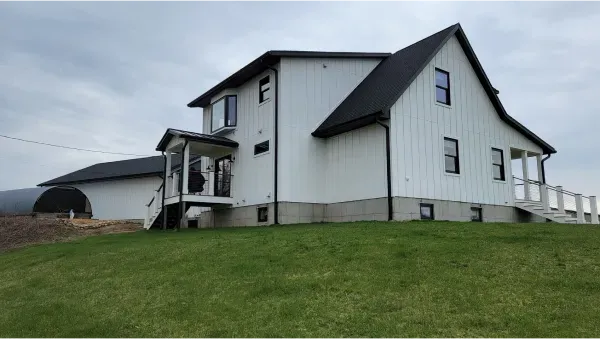 A large white house with a black roof is sitting on top of a lush green field.