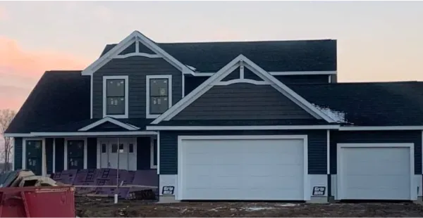 A large house with a black roof and white garage doors is being built.