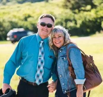 A man in a blue shirt and tie stands next to a woman in a denim jacket