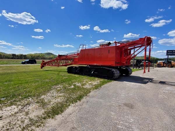 Red tracked crane on grass and pavement under a blue sky.