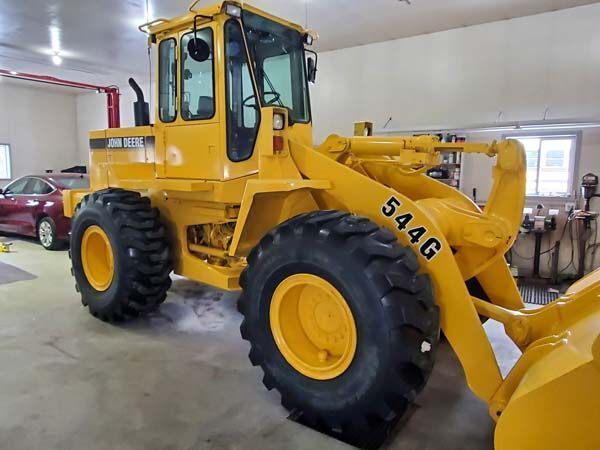 Yellow John Deere 544G wheel loader inside a garage.