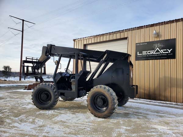 Black telescopic forklift parked in front of a tan building with the name