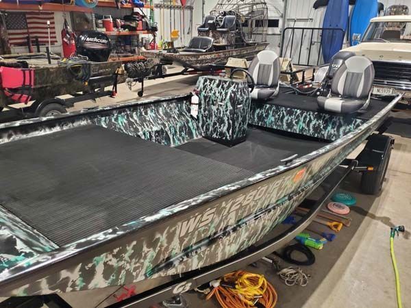Camouflage-wrapped fishing boat with black matting and two seats in a workshop setting.