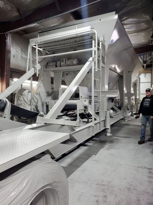 White industrial machine in a warehouse, man standing next to it.