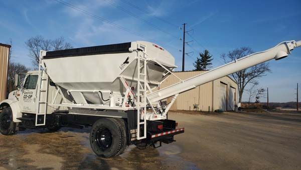 White truck with auger attached, used for distributing materials in an industrial setting.