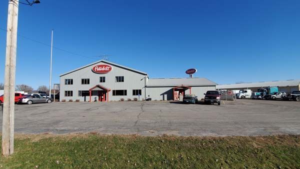 A Peterbilt dealership on a sunny day; gray building with red accents and logo, cars in the parking lot.