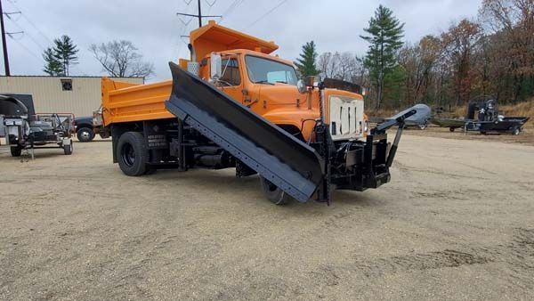 Orange snowplow truck parked on gravel lot.