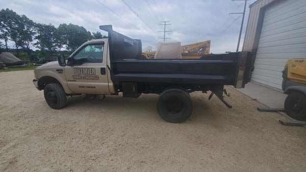 Beige dump truck parked outside a building. The truck has a black dump bed and black tires.