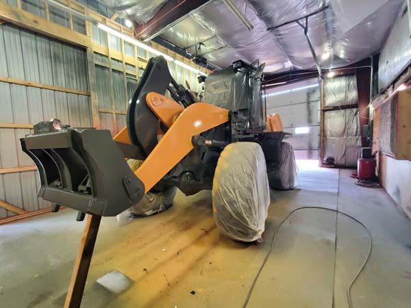 Orange and black front-end loader inside a partially constructed building.