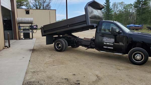 Black dump truck with raised bed, parked next to a building.