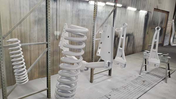 Suspension parts, including springs, coated in white paint inside a spray booth.