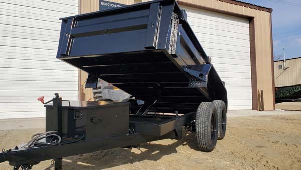 Black dump trailer with raised bed, outdoors near a building.