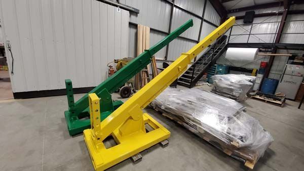 Two painted metal cranes, green and yellow, on wheels inside a warehouse.
