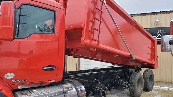 Red dump truck with raised bed, black frame, parked outdoors.