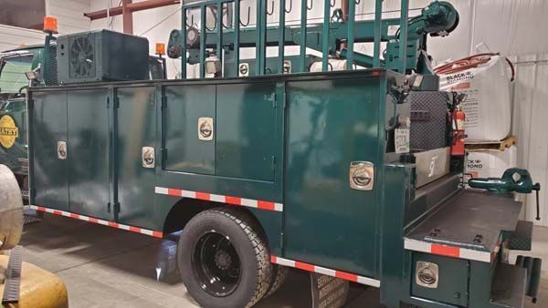 Green utility truck with compartments, lights, and a crane boom, indoors.