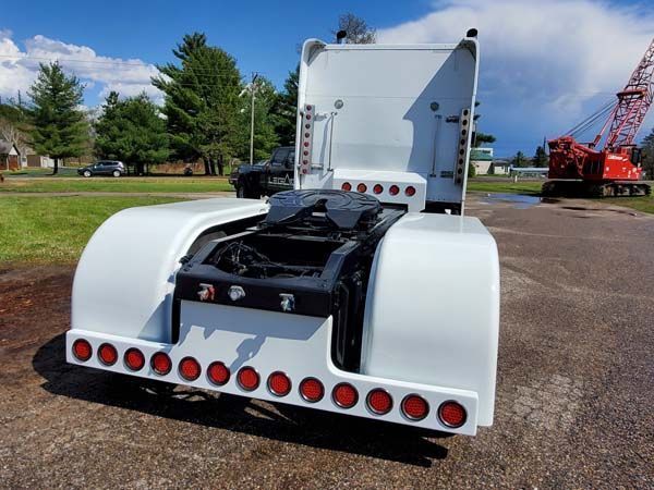 White semi-truck with red taillights, black hitch, parked outdoors on a sunny day.