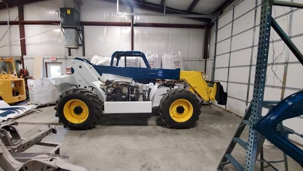 White and yellow industrial vehicle in a workshop, with a blue cab and roll cage.