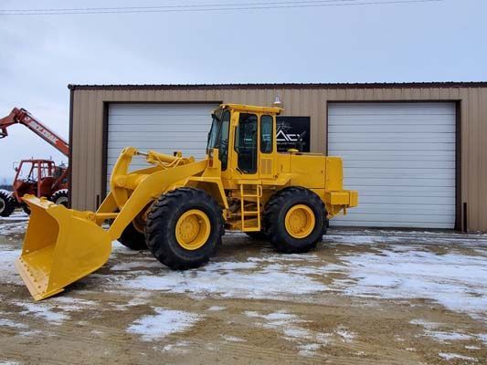 Yellow front-end loader parked in front of a building with two garage doors, snow on the ground.