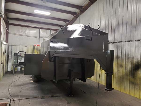 Dark gray trailer being painted in a spray booth.