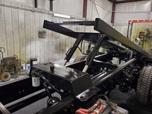 Black truck bed frame with hydraulic cylinders in a garage.