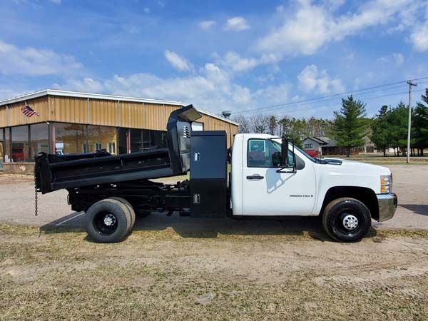 White dump truck parked in front of a wooden building on a sunny day.