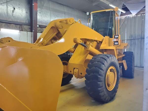 Yellow front-end loader inside a garage, with large tires and a raised bucket.