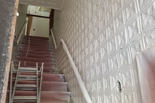 Staircase with white patterned walls, red carpet, metal handrails.