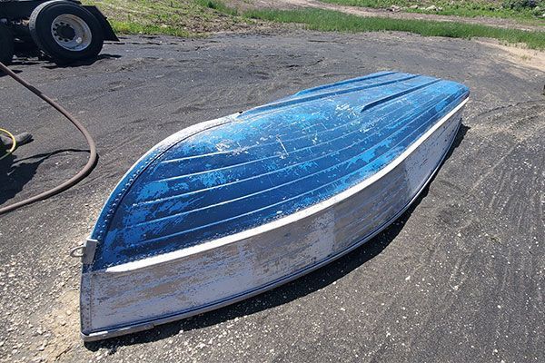 Blue and silver rowboat lying upside down on asphalt.