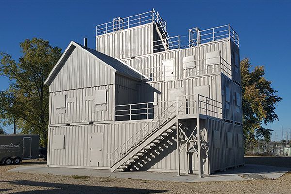 Fire training structure made of stacked shipping containers. Gray exterior, stairs, multiple doors and windows.