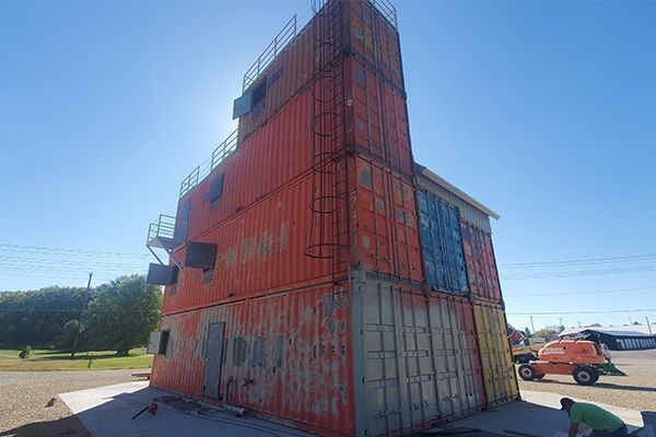 Fire training tower made of orange shipping containers under a sunny blue sky.