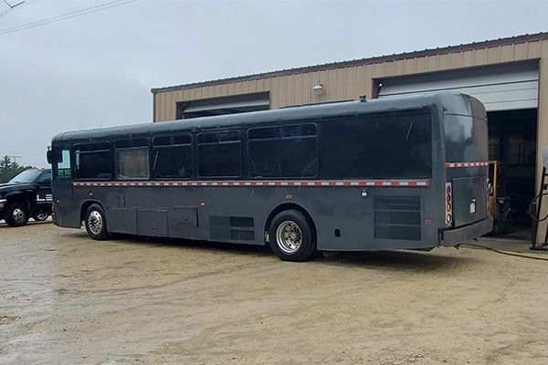 Gray bus parked outside a tan building with an open door, cloudy day.