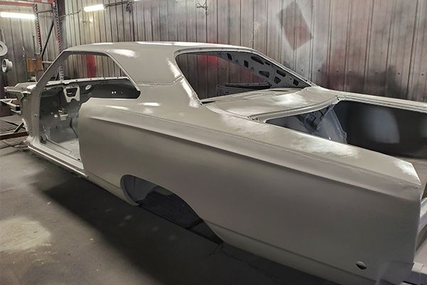 A light grey classic car body in a workshop, ready for paint.