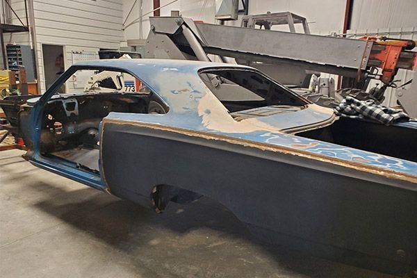 Blue classic car body in a workshop, partially disassembled, showing primer and original paint.