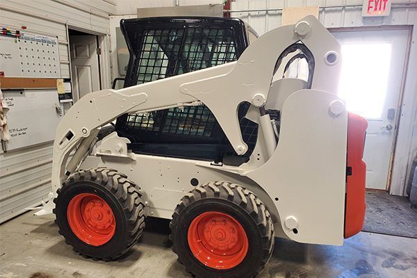 White Bobcat skid-steer loader with orange wheels, parked inside a garage.