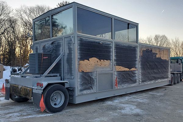 Gray industrial trailer with a glass-walled upper level, parked outdoors.