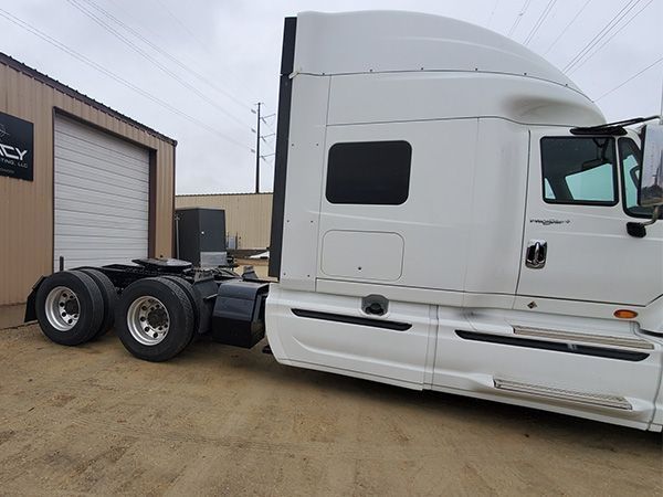 White semi-truck parked outside a building, tires visible, overcast sky.