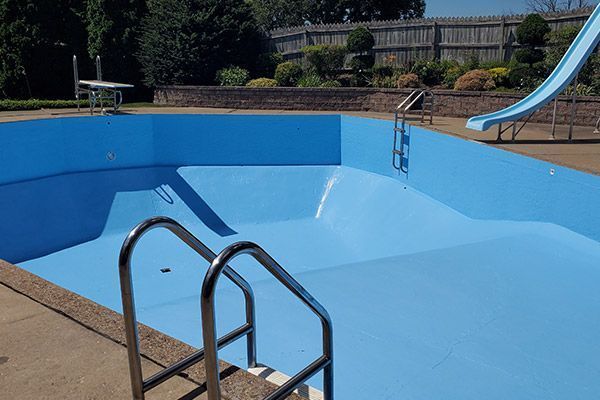 Empty blue swimming pool with chrome ladder and slide, in a backyard.