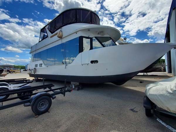 White houseboat on a trailer, outdoors, with blue sky and clouds.