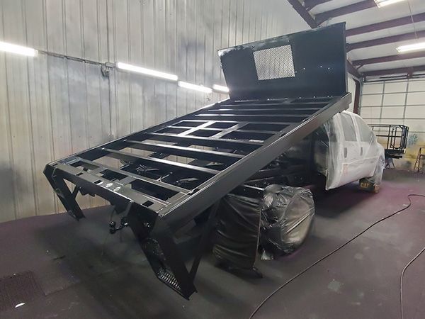 Black truck bed being painted in a spray booth.