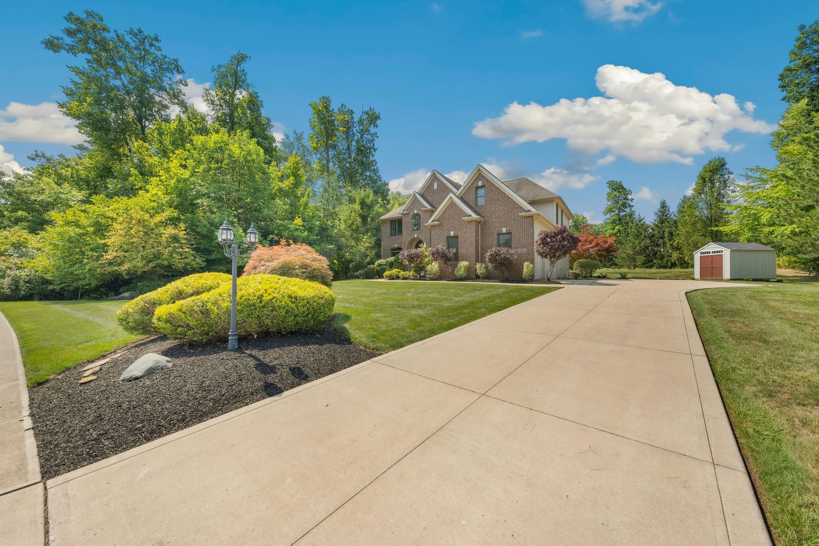 A driveway leading to a large house with a shed in the backyard.