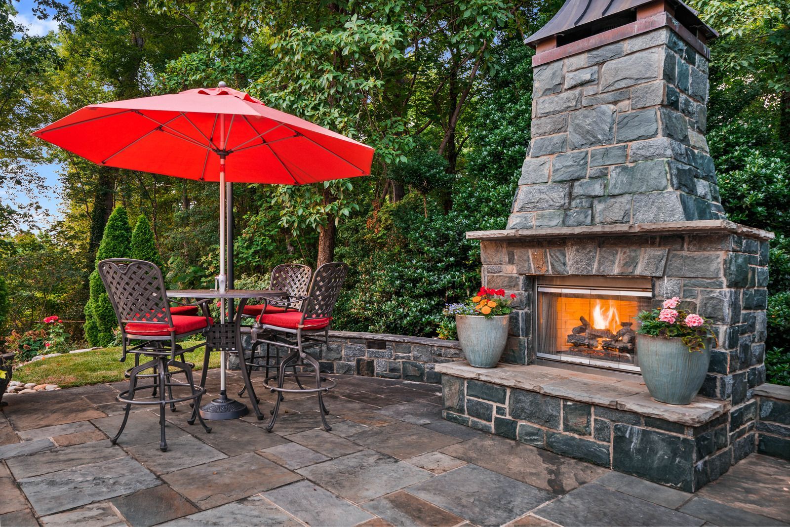 A patio with a fireplace , table and chairs and an umbrella.